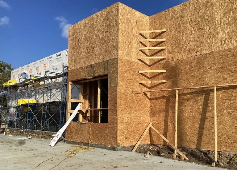 Construction site showing a building under development with cork or textured exterior walls, wooden framing, and scaffolding in background