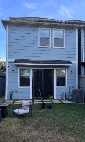 Modern light blue two-story house with white trim windows and black front door, featuring a small lawn and outdoor seating