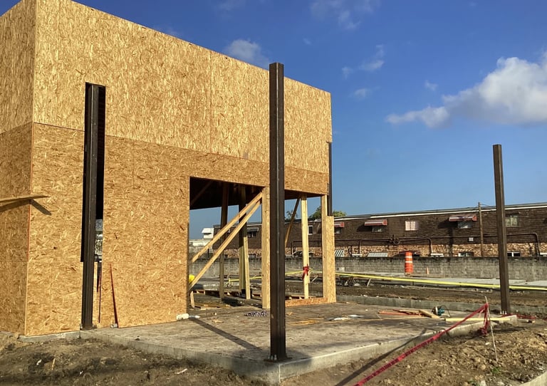 Wooden frame structure with OSB sheathing under construction against blue sky and industrial background