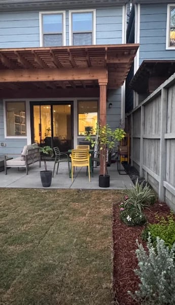 Modern home patio with covered pergola, seating area, glass doors, and manicured lawn with landscaping