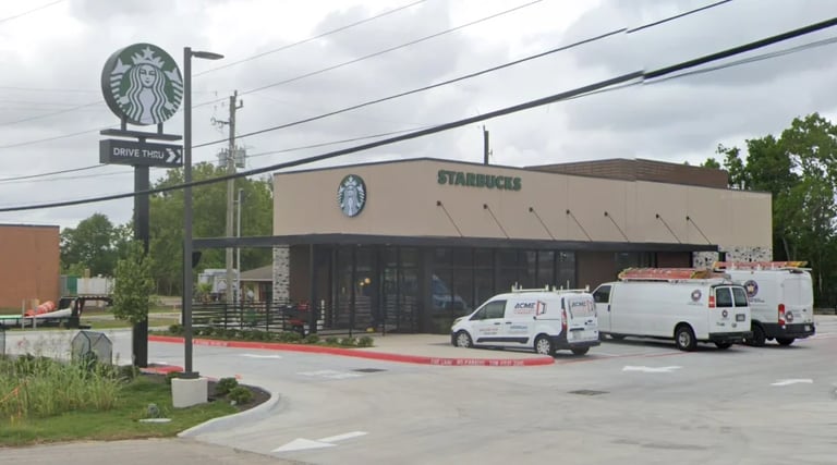Exterior view of a Starbucks coffee shop with green sign, entrance, and two vehicles parked in front lot on an overcast day