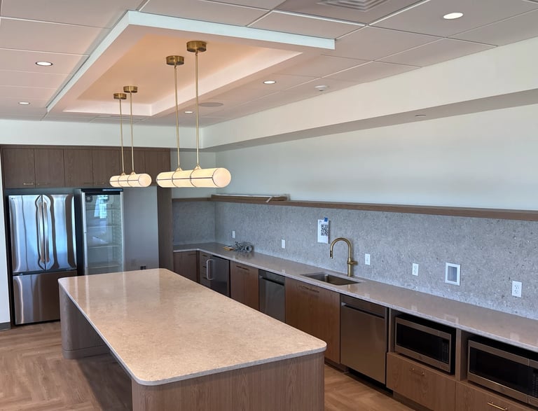Modern kitchen with large island, light stone countertop, dark wood cabinets, stainless steel appliances, and pendant lighting above