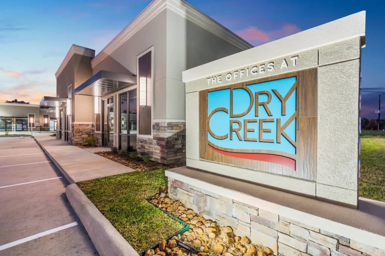 Dry Creek shopping center entrance with illuminated blue signage on stone monument at dusk with modern building facade visible in background