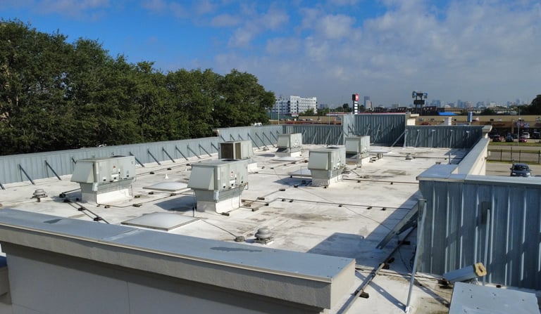 Flat commercial rooftop with HVAC units, vents, and equipment under construction, city skyline visible in background