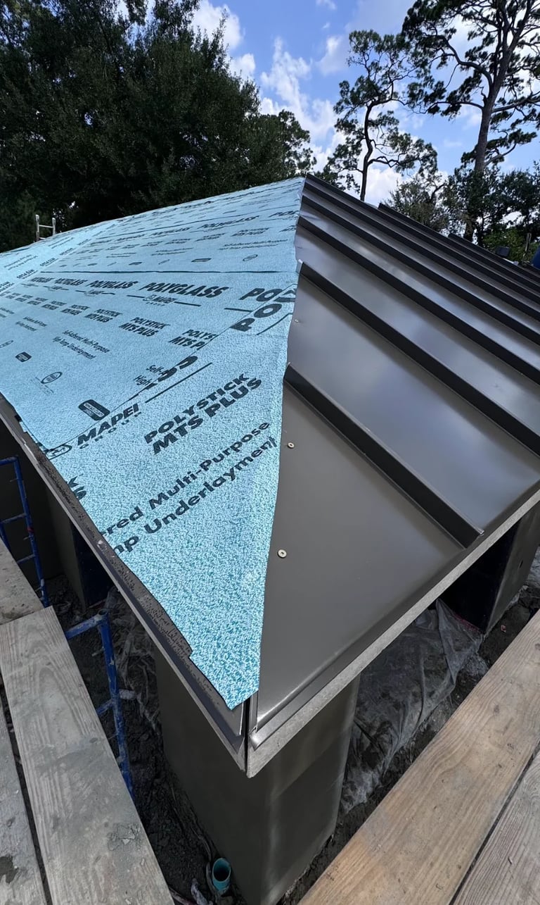 Roof installation with blue ice and water shield underlayment on gray metal guttering, surrounded by trees