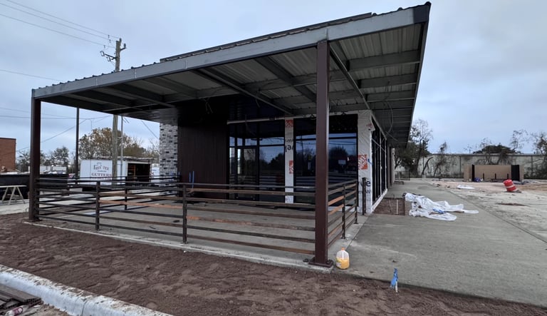 Modern metal-framed pavilion with horizontal railings and dark roof panels in an open yard area