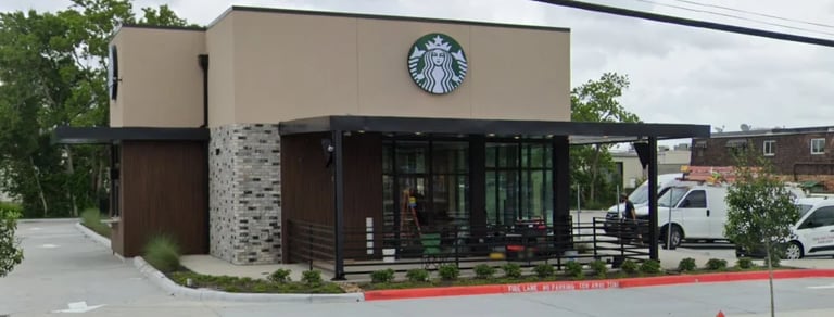 Starbucks storefront with modern beige and brown exterior, large Starbucks logo sign, and red striped curb in parking lot