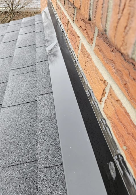 Close-up of a white gutter attached to a brick house next to asphalt roof shingles