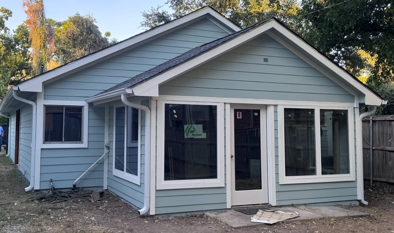 Modern light blue cottage with large front porch, white trim, black doors and windows, surrounded by trees