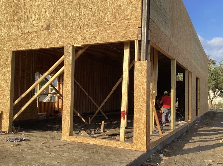 Construction of a large wooden frame building with open garage bays and a person in red shirt standing on the right