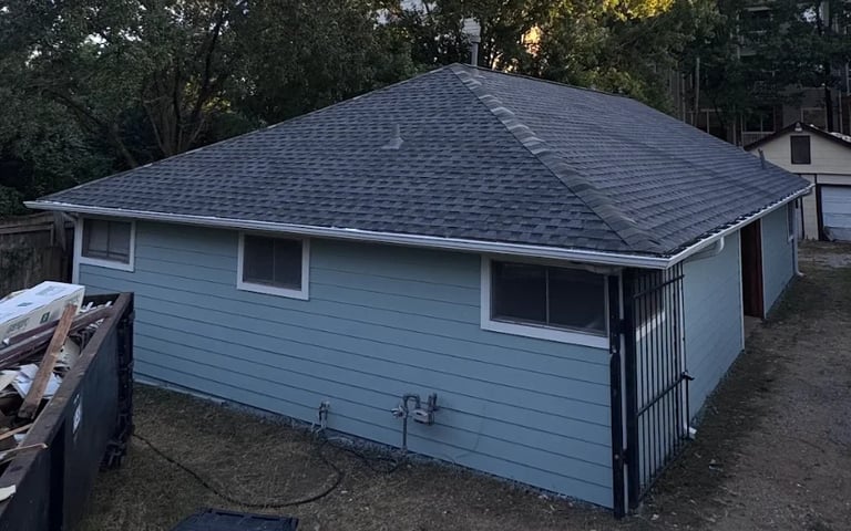 Light blue house with dark gray roof and white-trimmed windows surrounded by trees