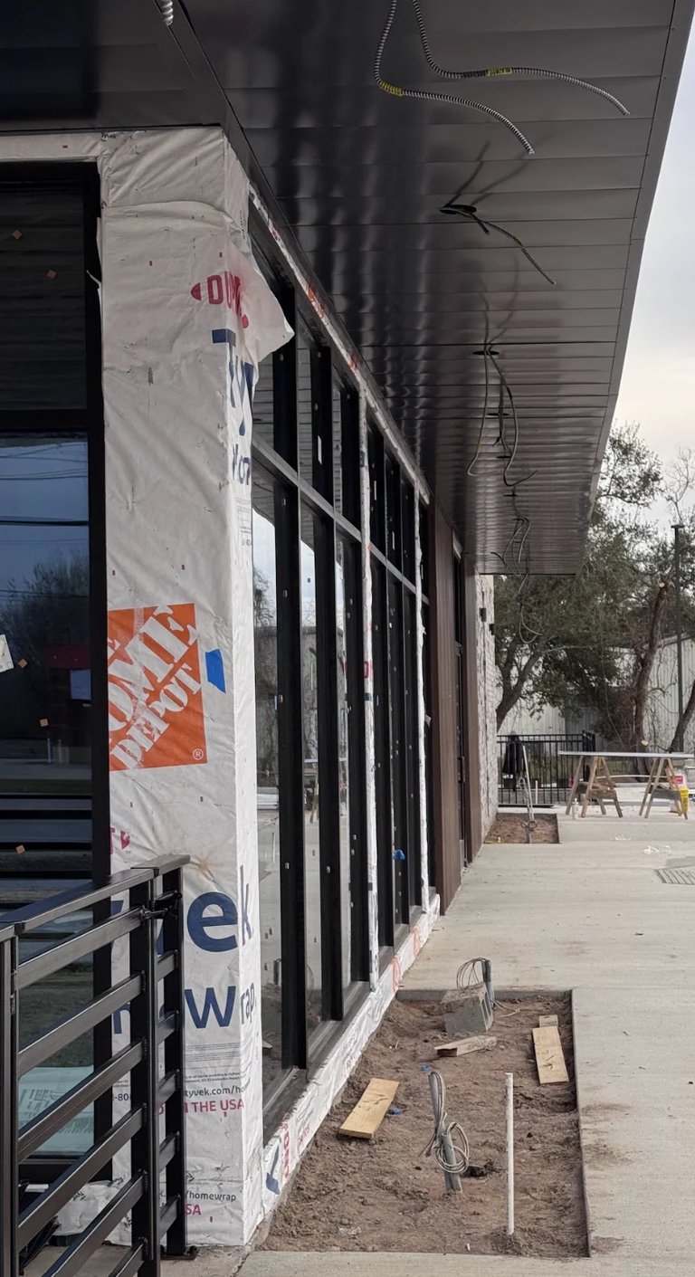 Exterior of building under construction with protective white wrap, Home Depot logo visible, metal railings and overhang visible
