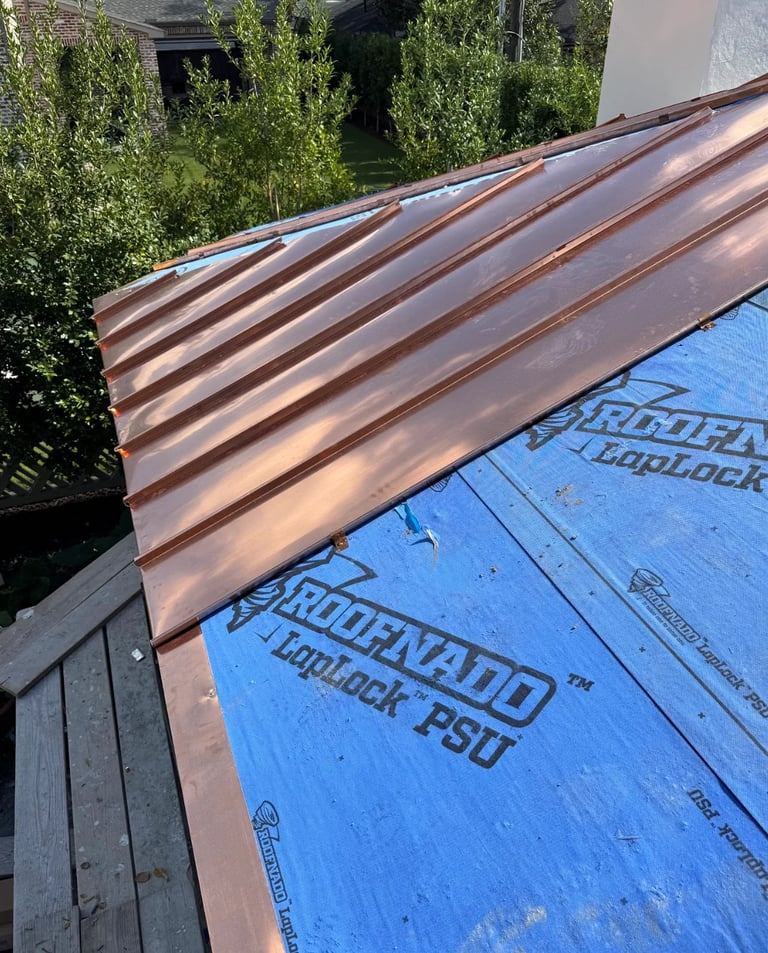 Corrugated metal roofing material leaning against blue house wrap during construction, with green shrubs in background
