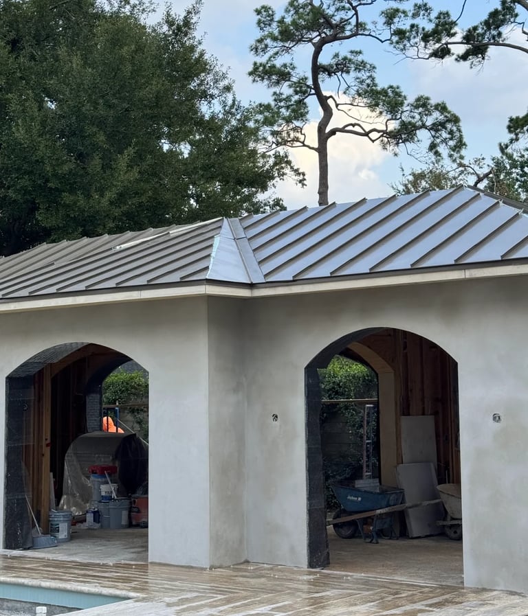 Modern white building with metal roof and two arched openings, surrounded by trees near a wooden deck