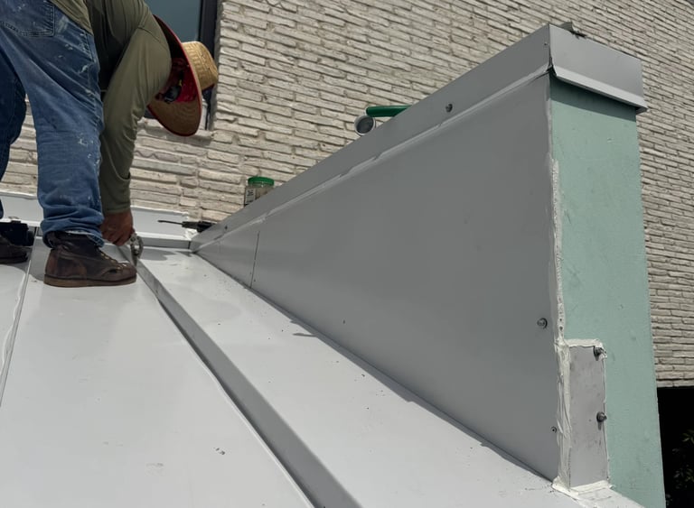 Worker installing gray metal flashing on white roof edge against brick wall building exterior