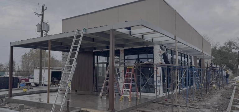 Commercial building under construction with metal framework, ladders, and scaffolding around the structure.