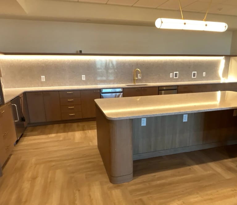 Modern office break room with wood cabinetry, island counter, and backlighting under upper shelves