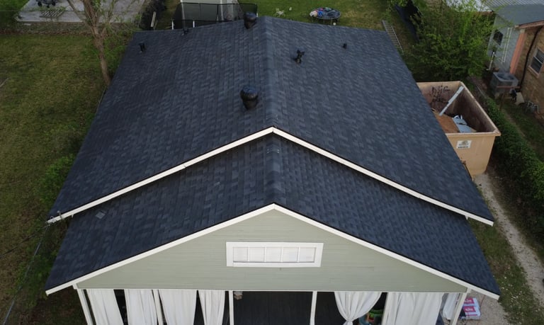 Aerial view of a residential home with dark asphalt shingle roof and white gabled entryway structure