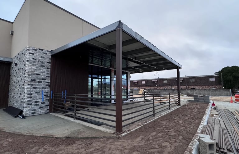 Modern equestrian facility with covered structure, metal railings, and white brick entrance building in rural setting