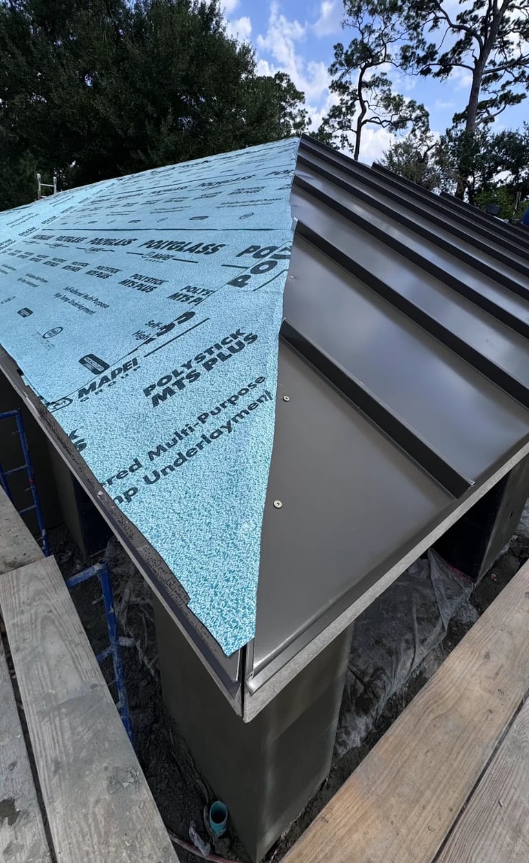 Roof installation with blue underlayment and metal flashing along the edge, trees visible in background