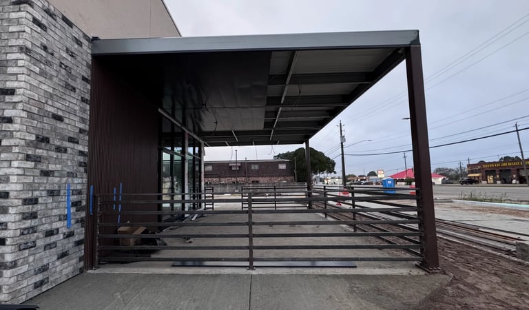Modern covered livestock loading area with metal gates and corrals, brick building to the left, rural farm setting visible in background