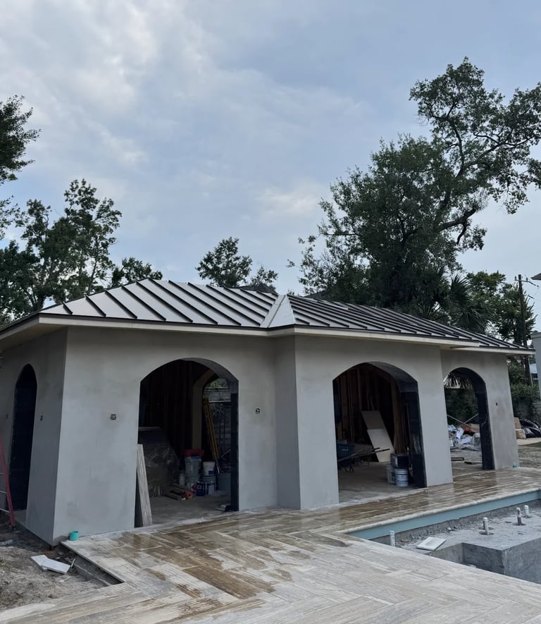 Modern white building with metal roof and arched entrances, surrounded by trees and wooden deck