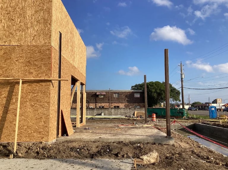 Construction site with new building framework, concrete foundation, metal support poles, and clear blue sky in background