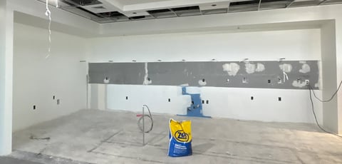 Construction site interior with yellow caution sign, exposed drywall, and ceiling work in progress